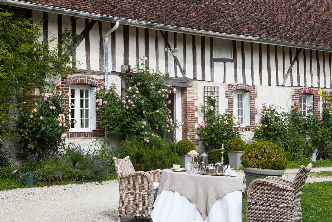 Seating area in front of farmhouse with climbing roses on façade