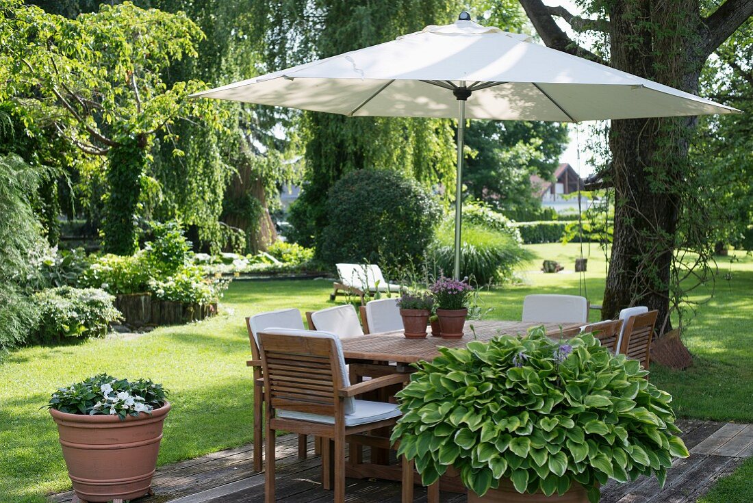 Sonnenschirm integriert in Gartentisch und Holzstühle mit weissen Polstern in sommerlichem Garten
