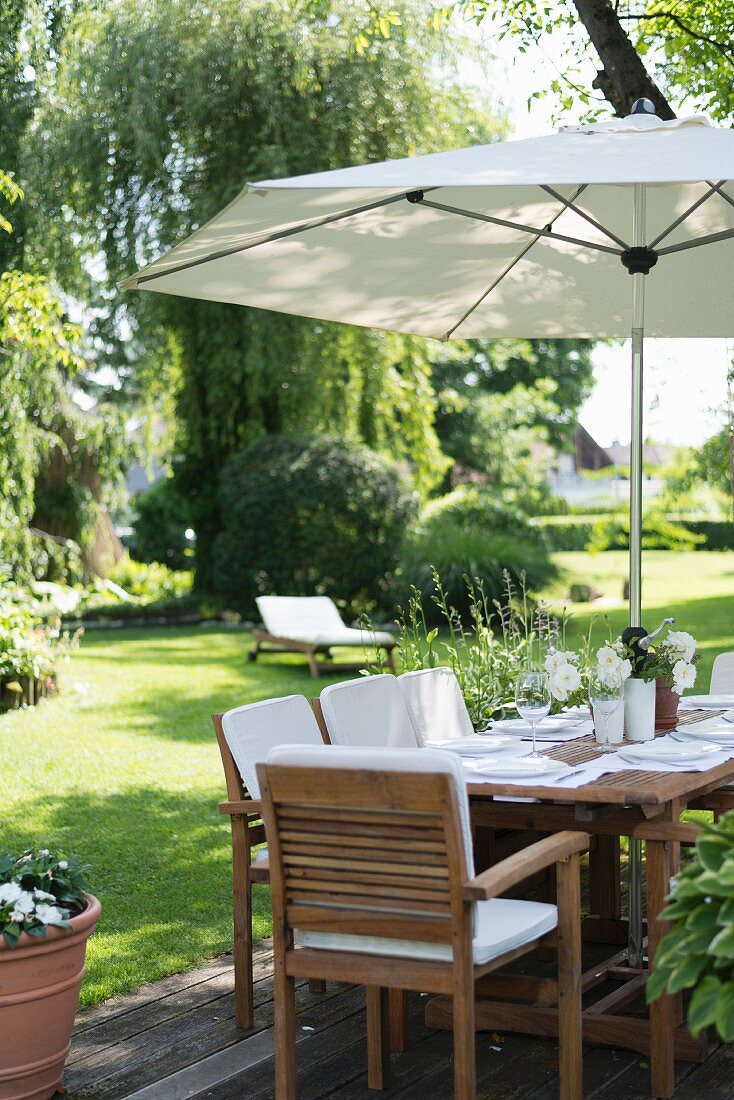 Gedeckter Tisch unter Sonnenschirm in gepflegtem Garten