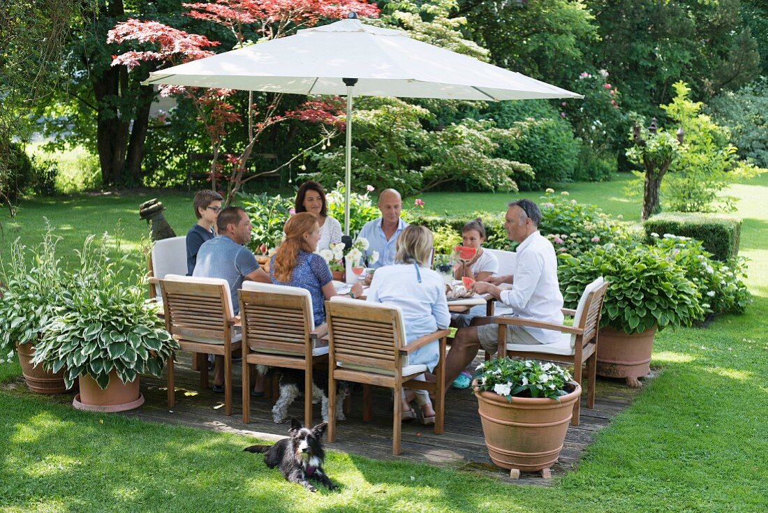 Gäste an gedecktem Tisch unter Sonnenschirm im Garten