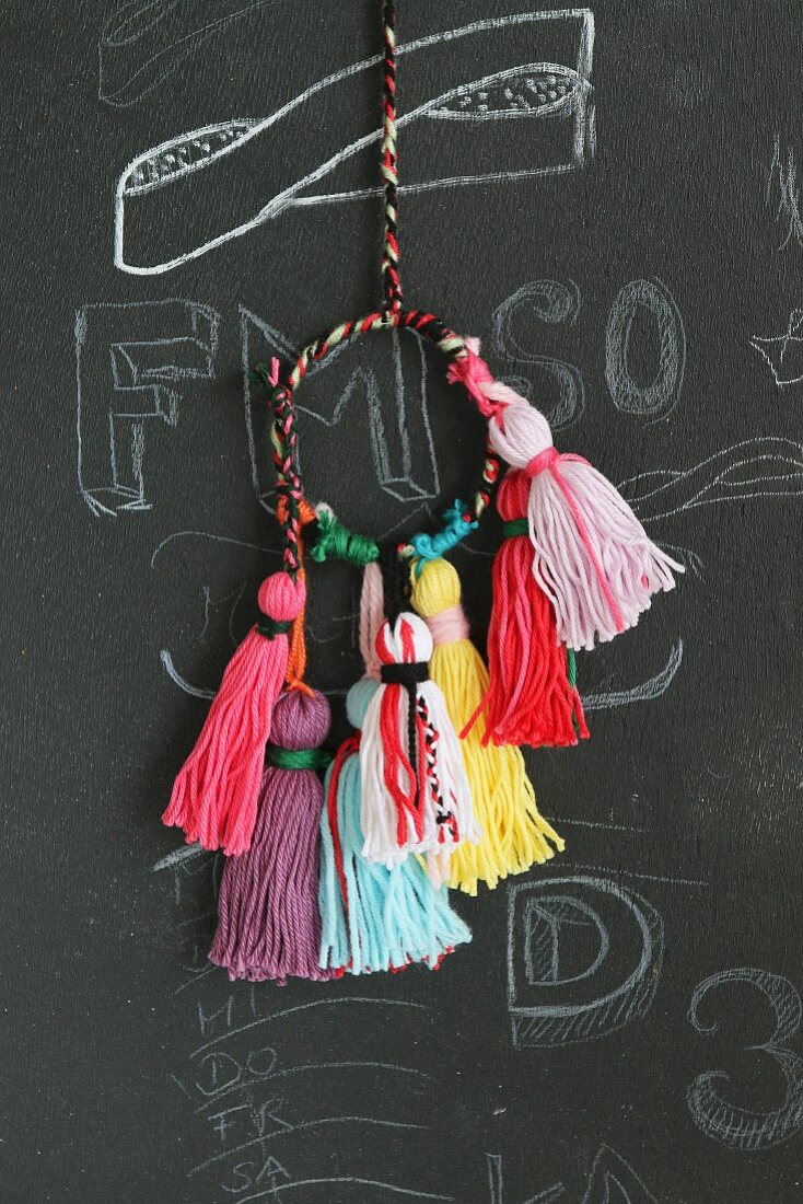 Colourful woollen tassels for key chains hanging against chalkboard