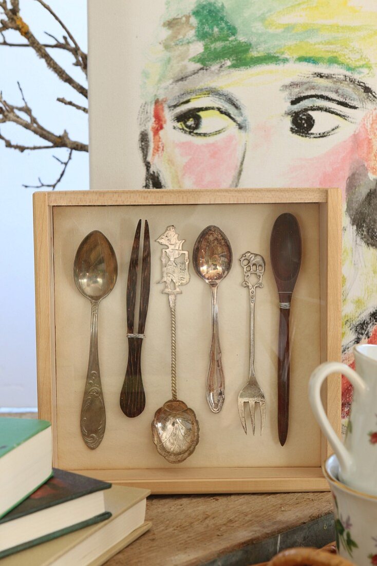 Cutlery mounted in wooden box in front of modern portrait on canvas