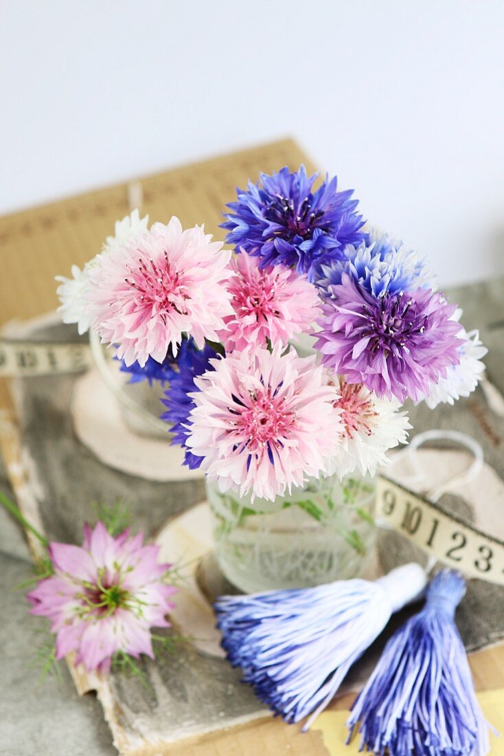 Posy of pastel cornflowers in glass vase decorated with tassels