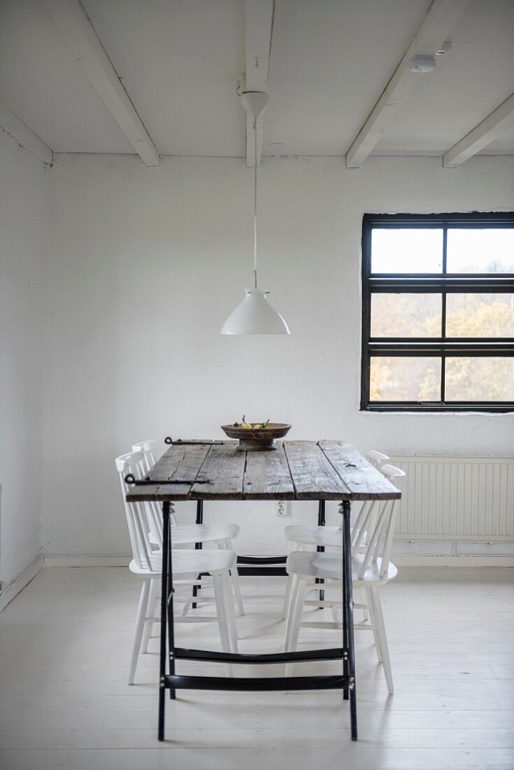 White-painted chars around wooden table on metal trestles in simple dining area