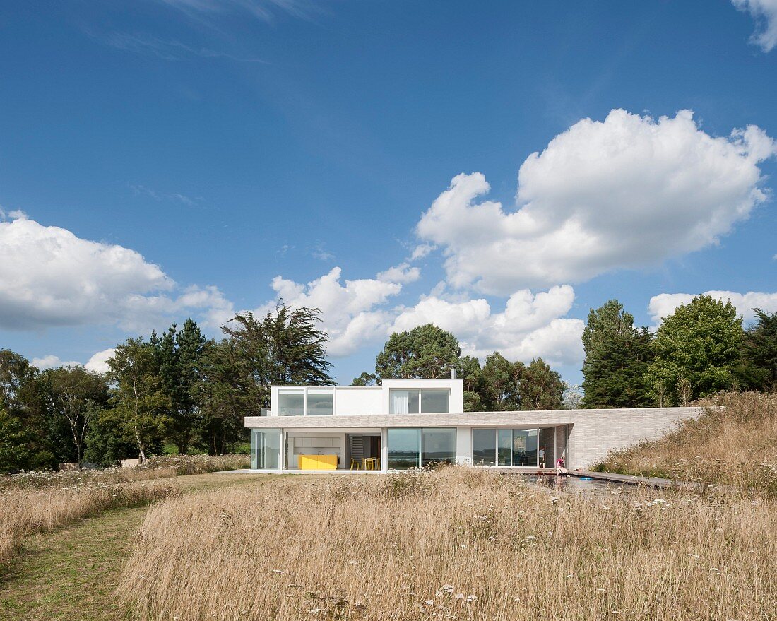 Modern architect-designed house with flat roofs and large windows seen across meadow