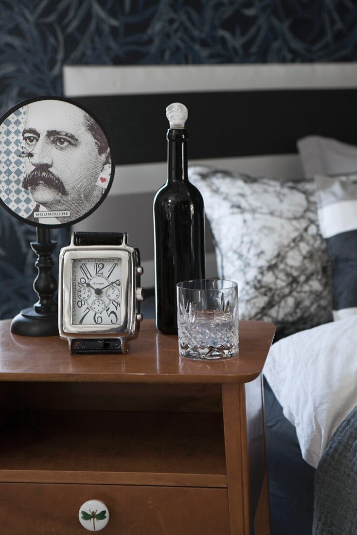Flasche und Glas neben Wecker und Vintage Tischlampe mit Männerportrait auf Nachttisch