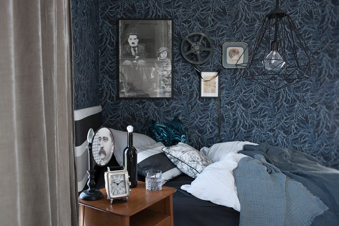 Nachttisch und Bett vor floraler Mustertapete mit 'Charlie Chaplin'-Poster und Filmrolle