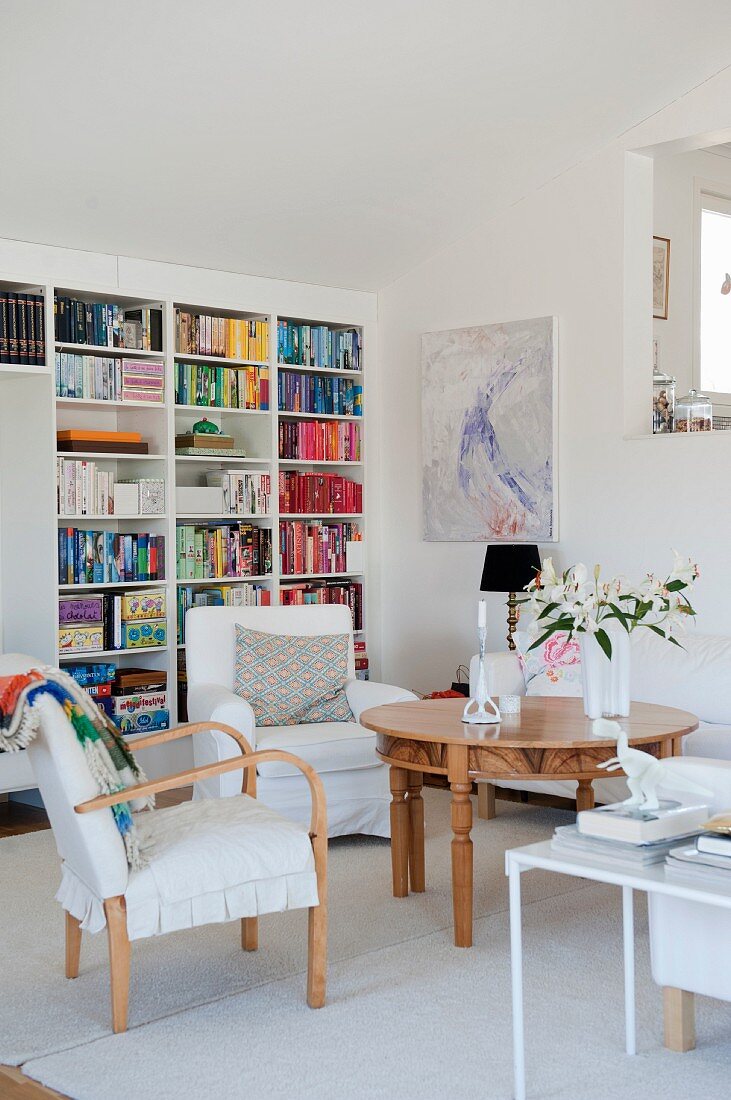 Moderner Wohnbereich mit Sesseln um runden Holztisch mit geschnitzten Beinen, im Hintergrund Bücherwand