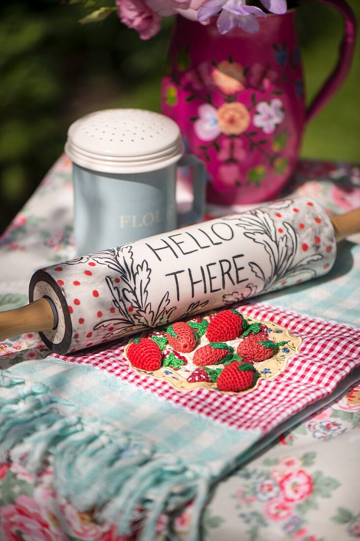 Beschriftetes Wellholz und Tischdecke mit gehäkelten Erdbeeeren auf nostalgisch dekoriertem Gartentisch