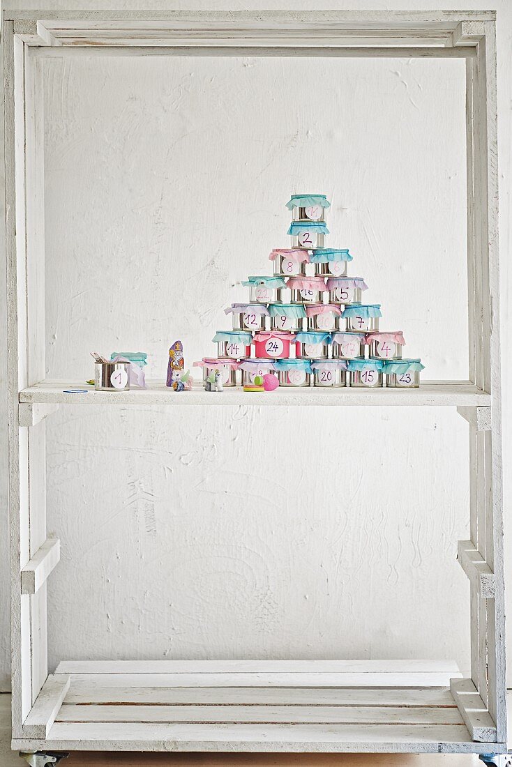 Advent calender hand-made from decorated tin cans in white-painted wooden frame