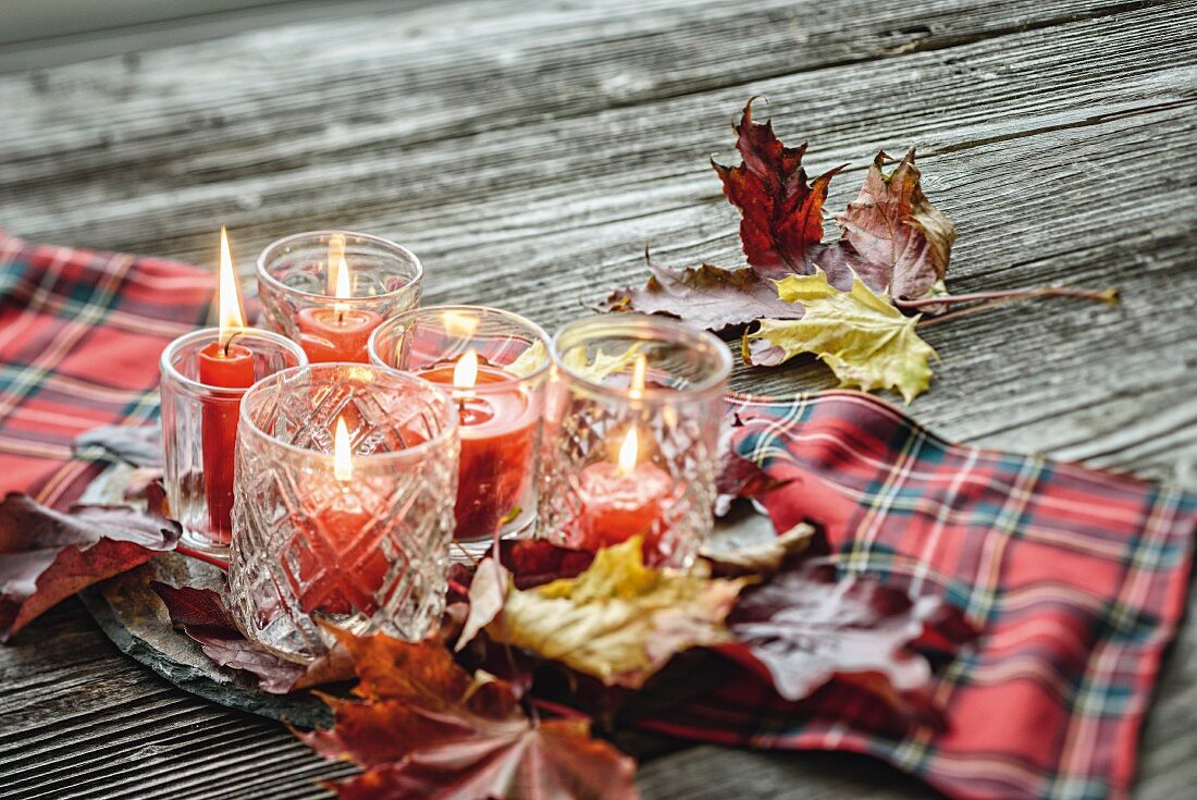 Windlichter mit roten Kerzen auf einem Karostoff mit Herbstlaub