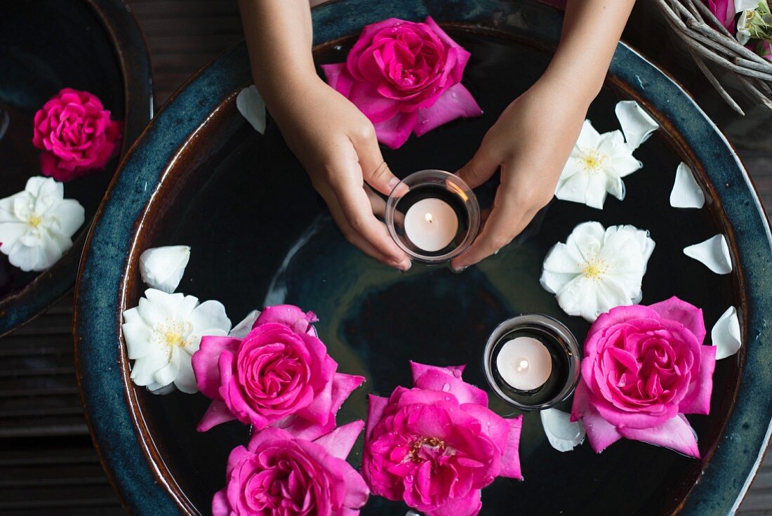 Roses and tealights floating in ceramic bowl and tealight held in girl's hands