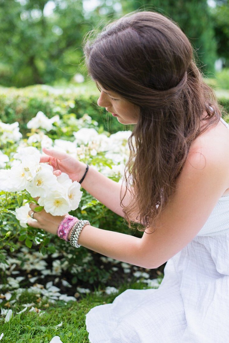 Junge Frau betrachtet weiße Rosen im Garten