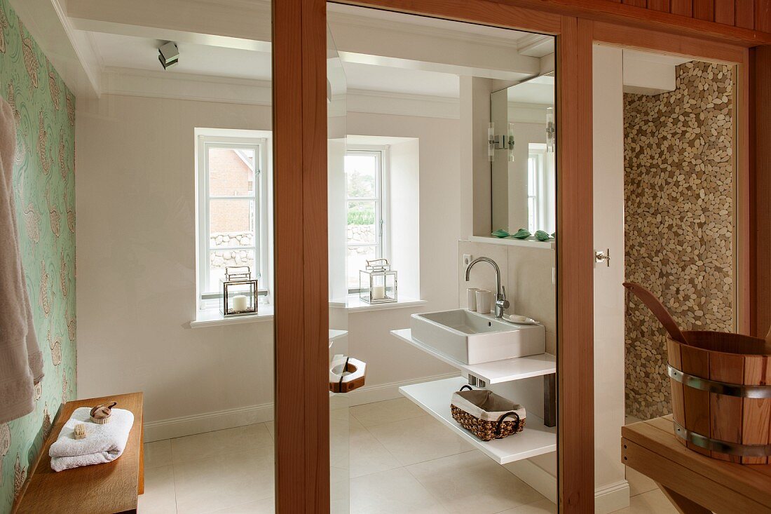 Blick durch geöffnete Glastür in modernes Bad, seitlich Waschtisch mit Ablagen