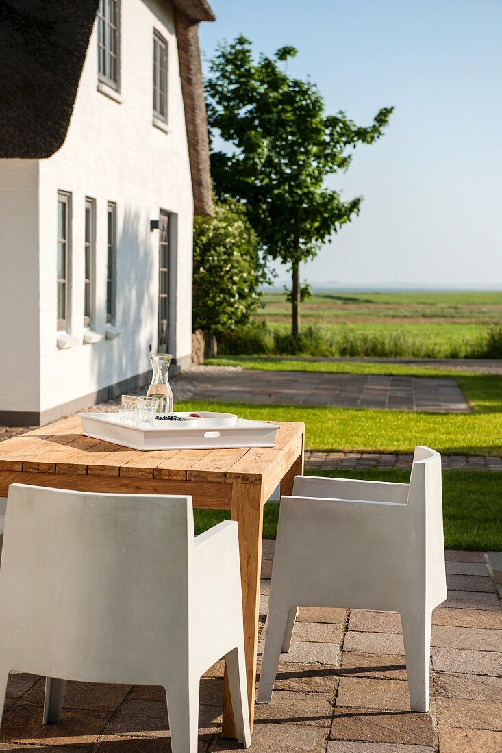 White, plastic, modern outdoor chairs and wooden table on summery terrace outside holiday home
