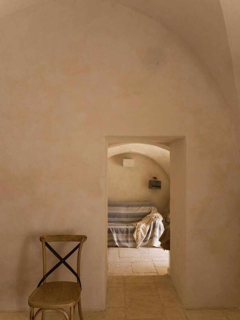 Spärlich möblierter Gewölberaum mit Natursteinboden, Durchgang und Blick auf Sofa mit Plaid; mediterranes Flair