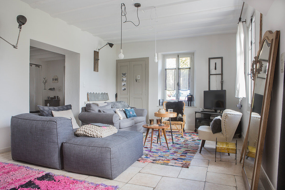 Grauer Polstersessel mit passendem Hocker und Retro Sessel um Beistelltische im Wohnbereich, gemusterte Teppiche auf Fliesenboden