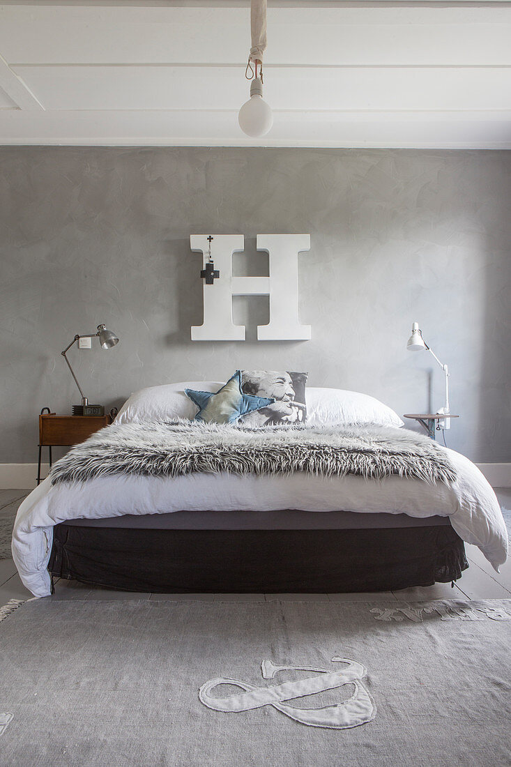 Fur blanket on bed below large white decorative letter on grey stucco lustro wall