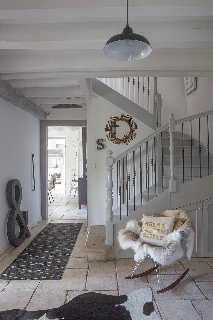 Klassiker Schaukelstuhl mit Tierfell vor grauem Treppenaufgang in restauriertem Hausflur