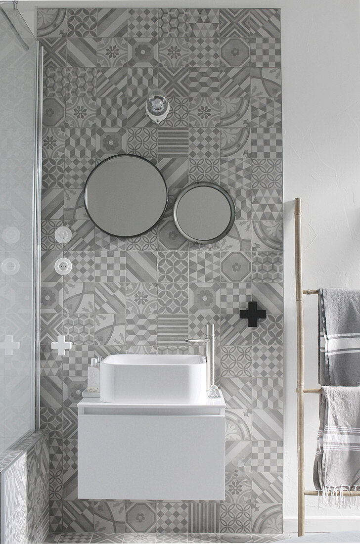 Modernes weißes Waschbecken mit Unterschrank an Wandstreifen mit grauen Ornamentfliesen