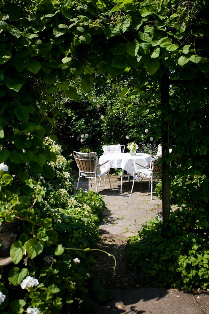 Blick auf sommerlichen, romantischen Gartenplatz mit Tisch und Stühlen in einer Laube