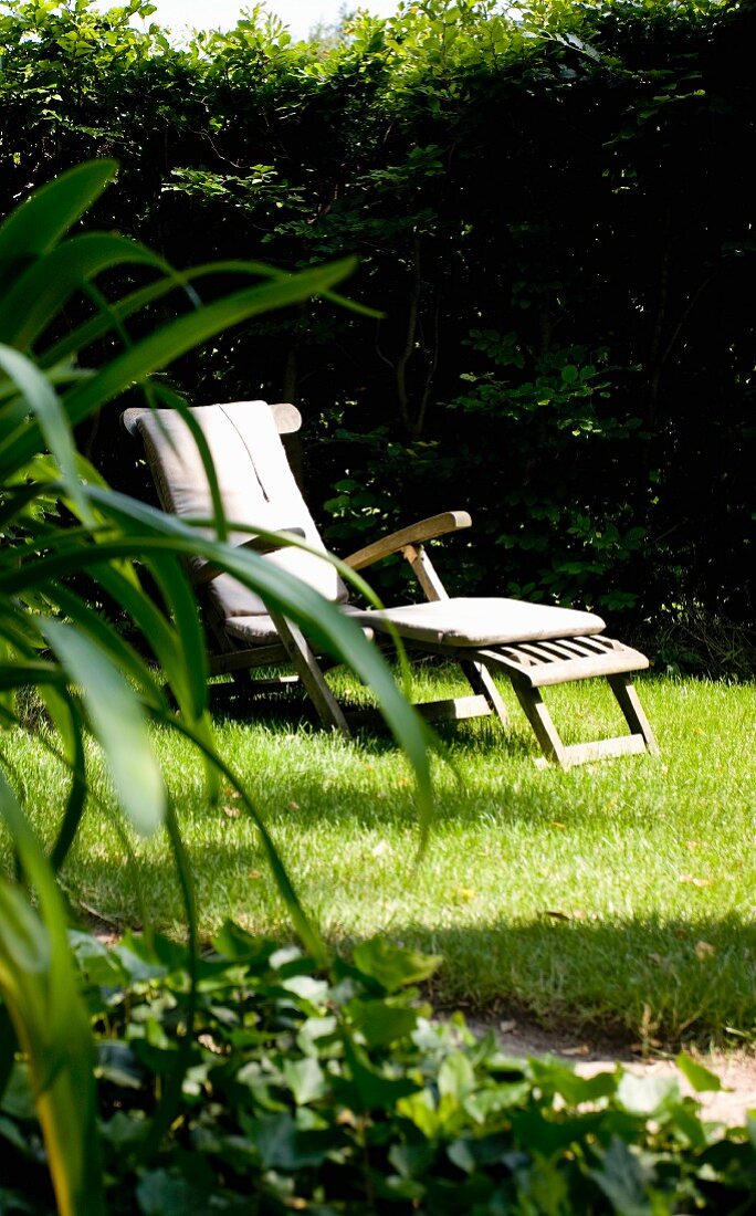 Holzliegestuhl auf Rasen in sommerlichem Garten