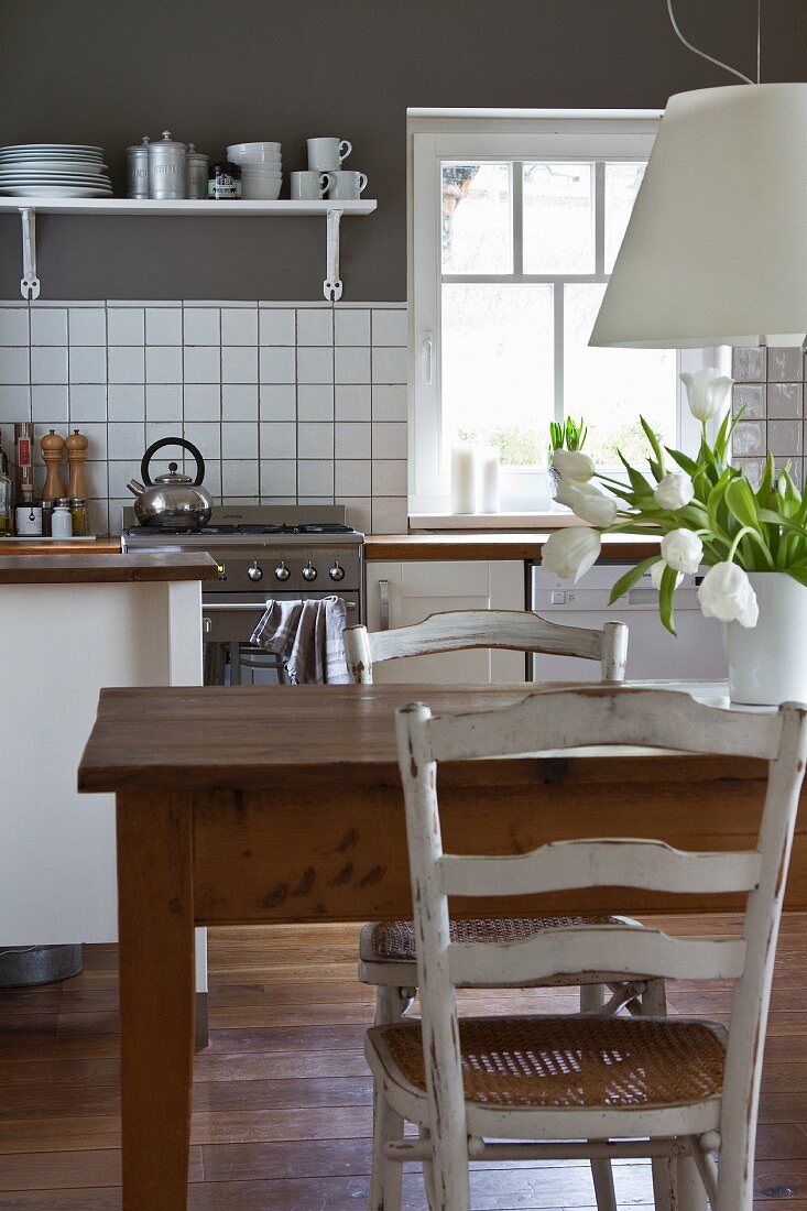 Old wooden table below white pendant lamp in modern kitchen with white counter against grey wall