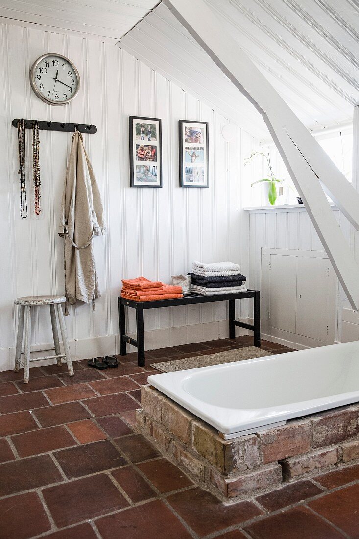 Ländliches Bad mit weisser Holzverkleidung an Wand und Decke, in Terrakottaboden eingelassene Badewanne mit Ziegeleinfassung