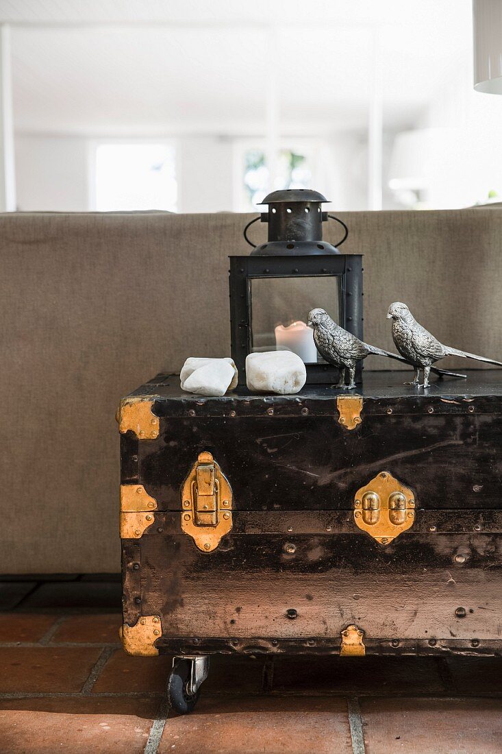 Metal birds, stones and lantern on vintage-style trunk with castors and metal fittings