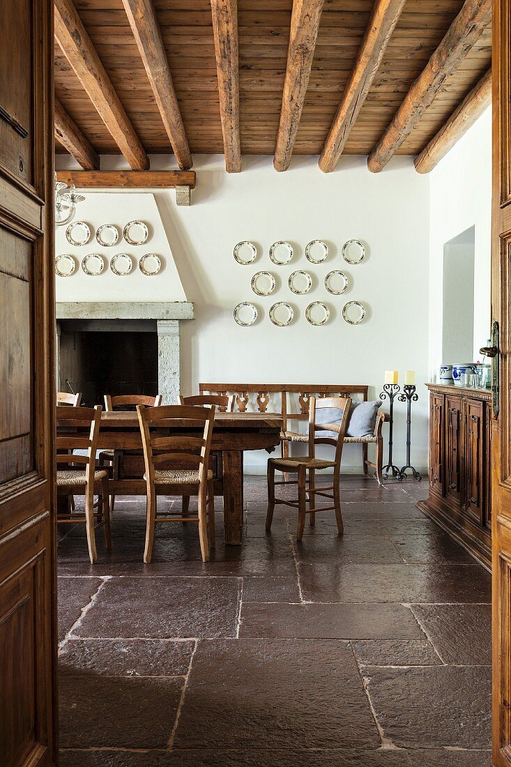 Wooden table and chairs in traditional dining room with rustic stone floor and wood-beamed ceiling