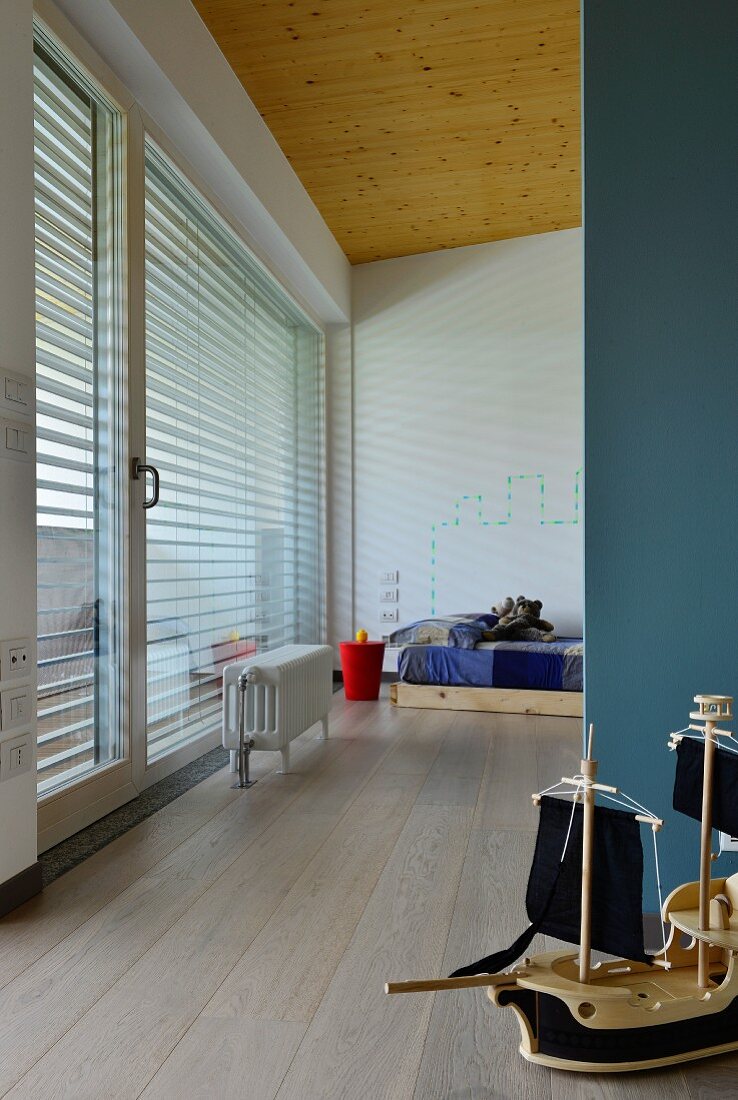 Modellboot vor blauer Wandscheibe und Blick auf minimalistisches Kinderzimmer in Designerwohnung