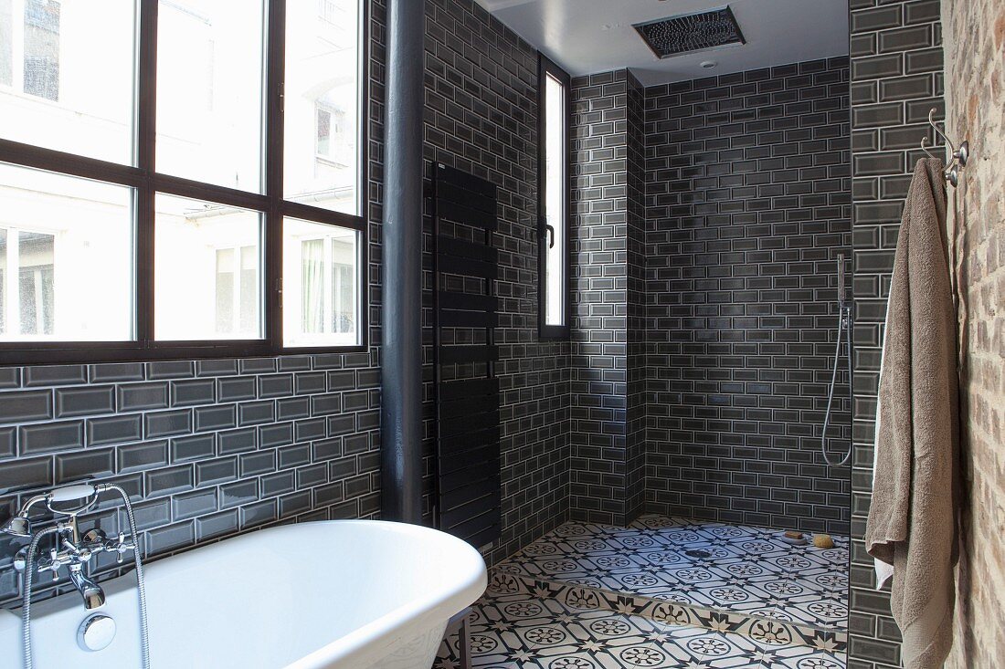 White bathtub below industrial window and shower area with ornate tiles