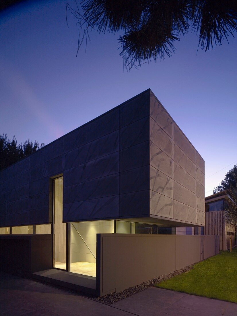 Exterior view of cubic house with illuminated glass walls and overhanging upper section