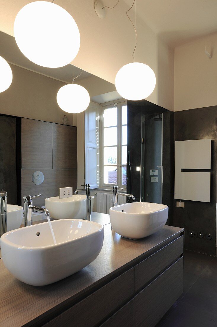Twin sinks on washstand below large mirror and spherical lamps in bathroom