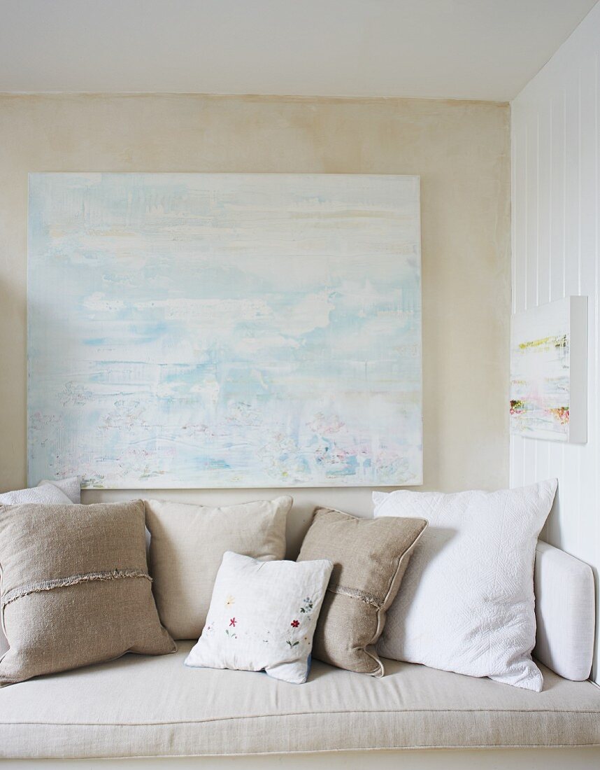 Sitzbank mit Kissen in Weiß und Naturfarben, vor Wand mit modernem Bild