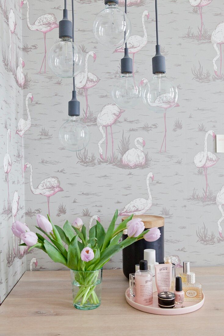 Pendelleuchten, Tulpen und Kosmetik vor einer Tapete mit Flamingos