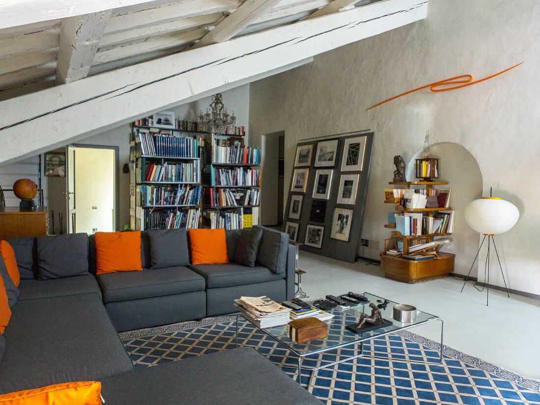 Wohnzimmer mit schrägem Dach und Sichtbalken, graues Sofa und verschiedene Regale