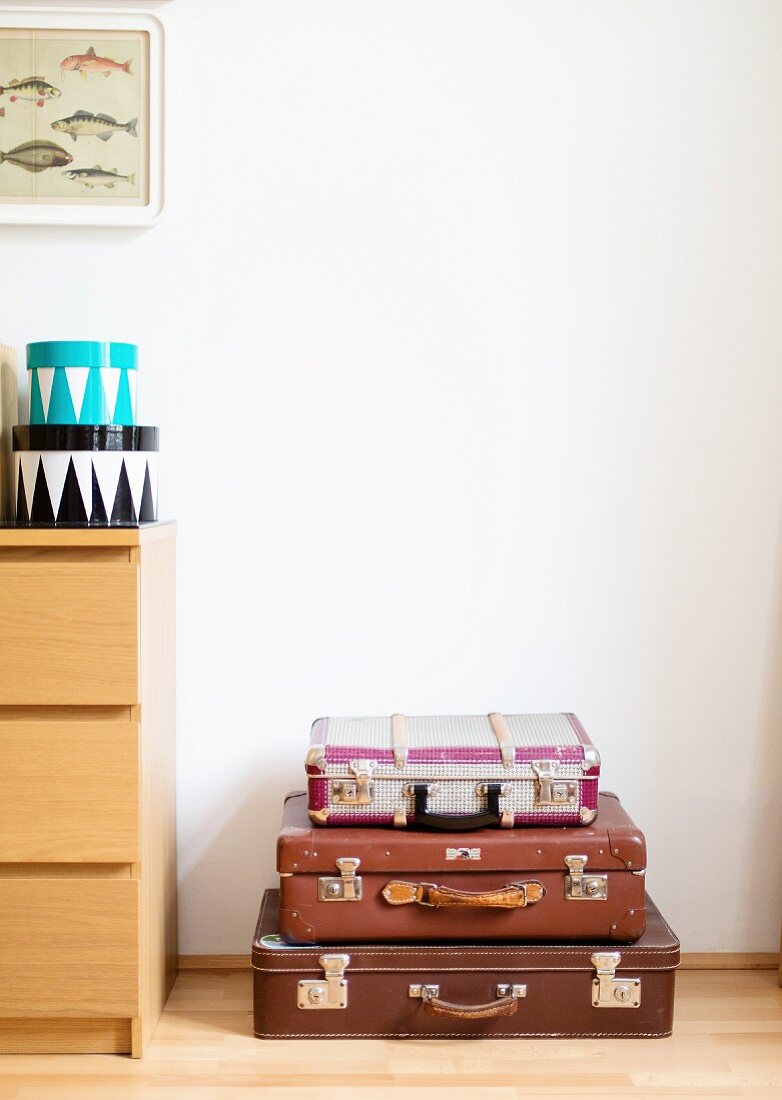 Stack of vintage suitcases next to chest of drawers with round boxes on top