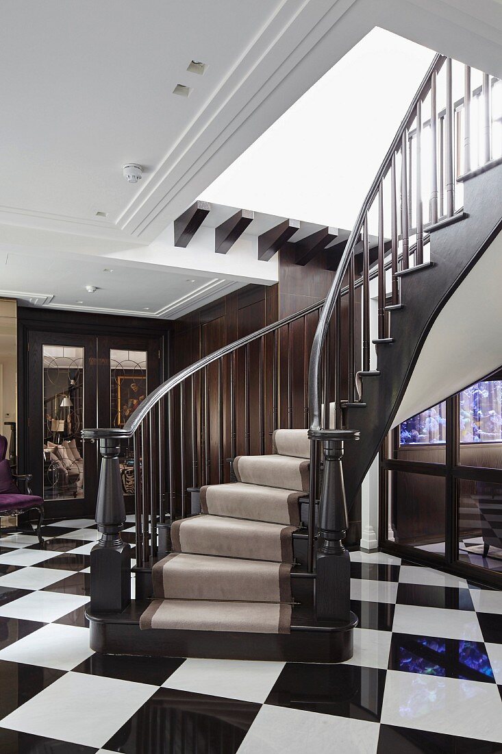 Eingangsbereich mit elegant geschwungene Treppe auf schwarz-weißem Schachbrettboden
