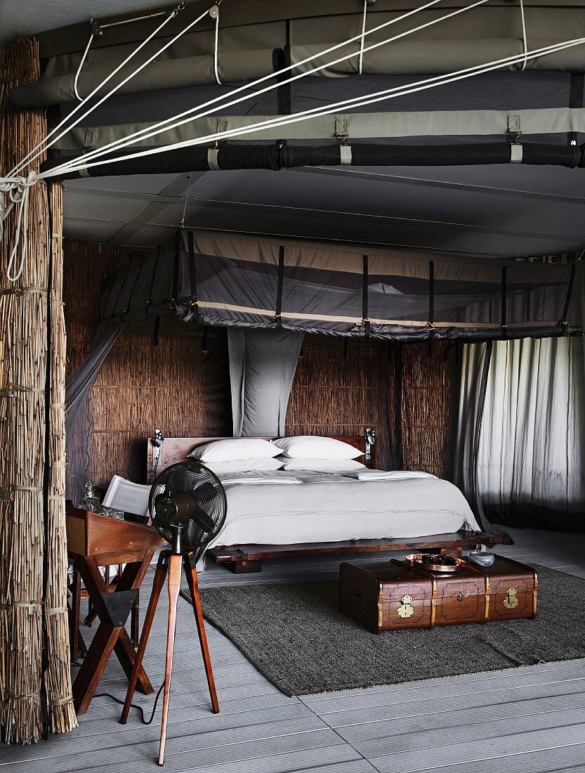 Schlafzimmer in afrikanischem Stil, mit Strohwänden und modernem Moskitobaldachin