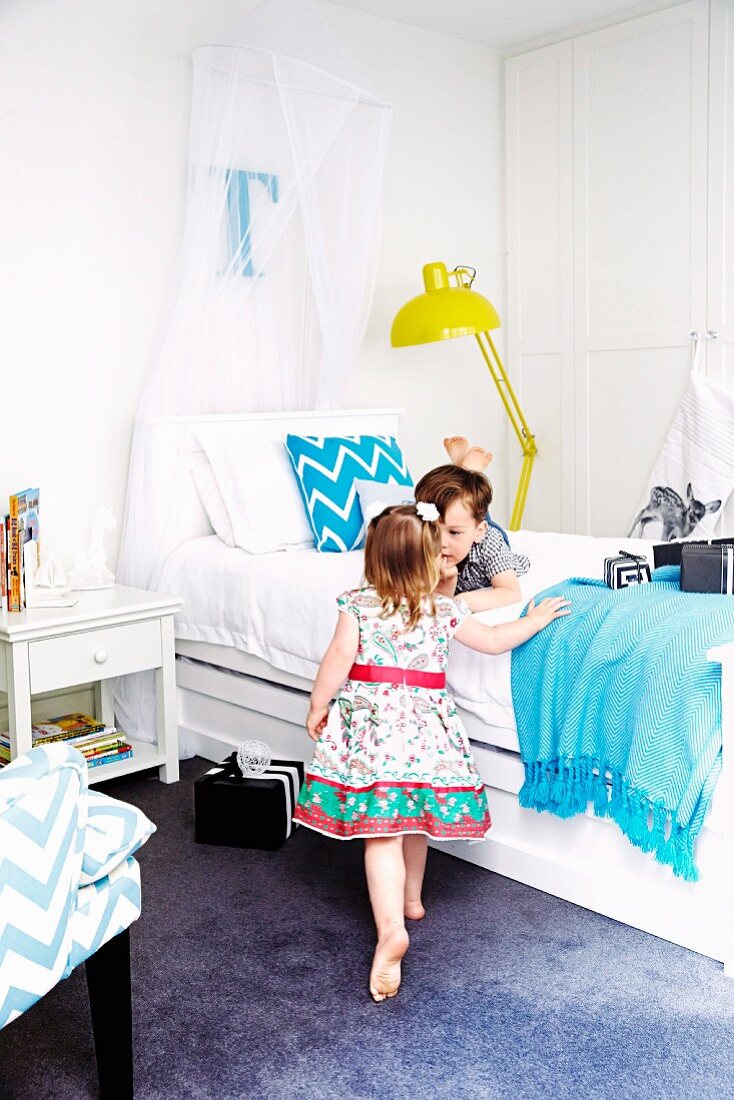 Kinder mit verpackten Geschenken in Schlafzimmer mit weißen Betten und elegantem Flair