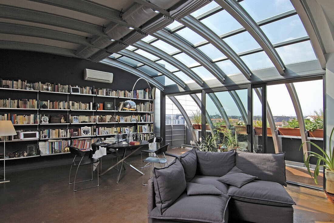 Bookcase, dining area and lounge in open-plan living area with metal and glass elements