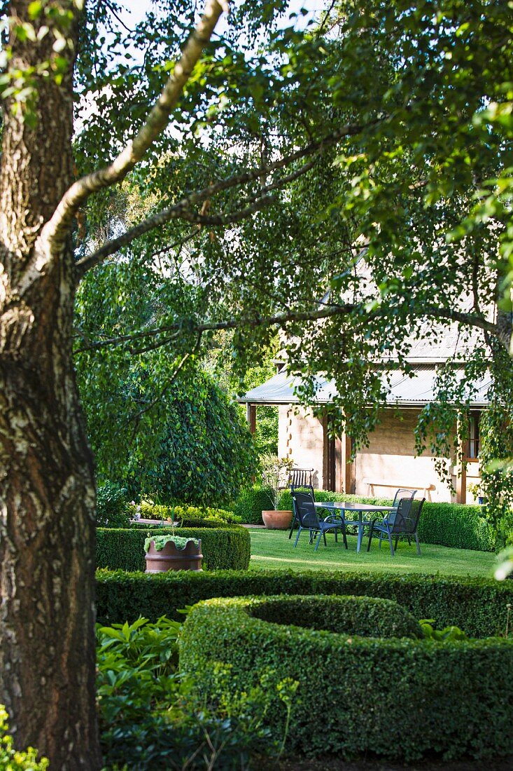 Blick in sommerlichen Garten mit spiralförmiger Buchshecke, Sitzplatz vor Wohnhaus