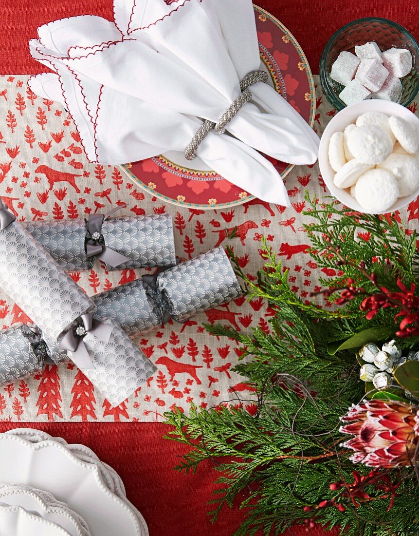 Gebäck in Schalen neben Teller mit Stoffservietten und Silberring auf weihnachtlich geschmücktem Tisch