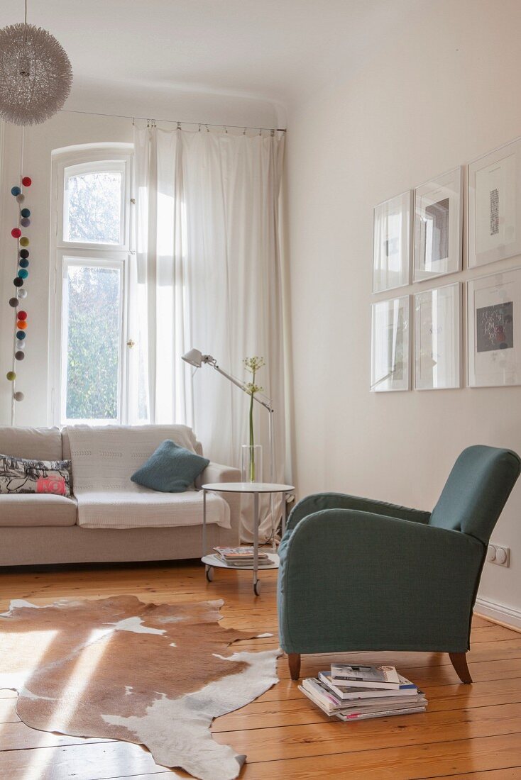 Wohnzimmerecke mit Armlehnsessel, Dielenboden mit Tierfellteppich und Sofa vor Fenster