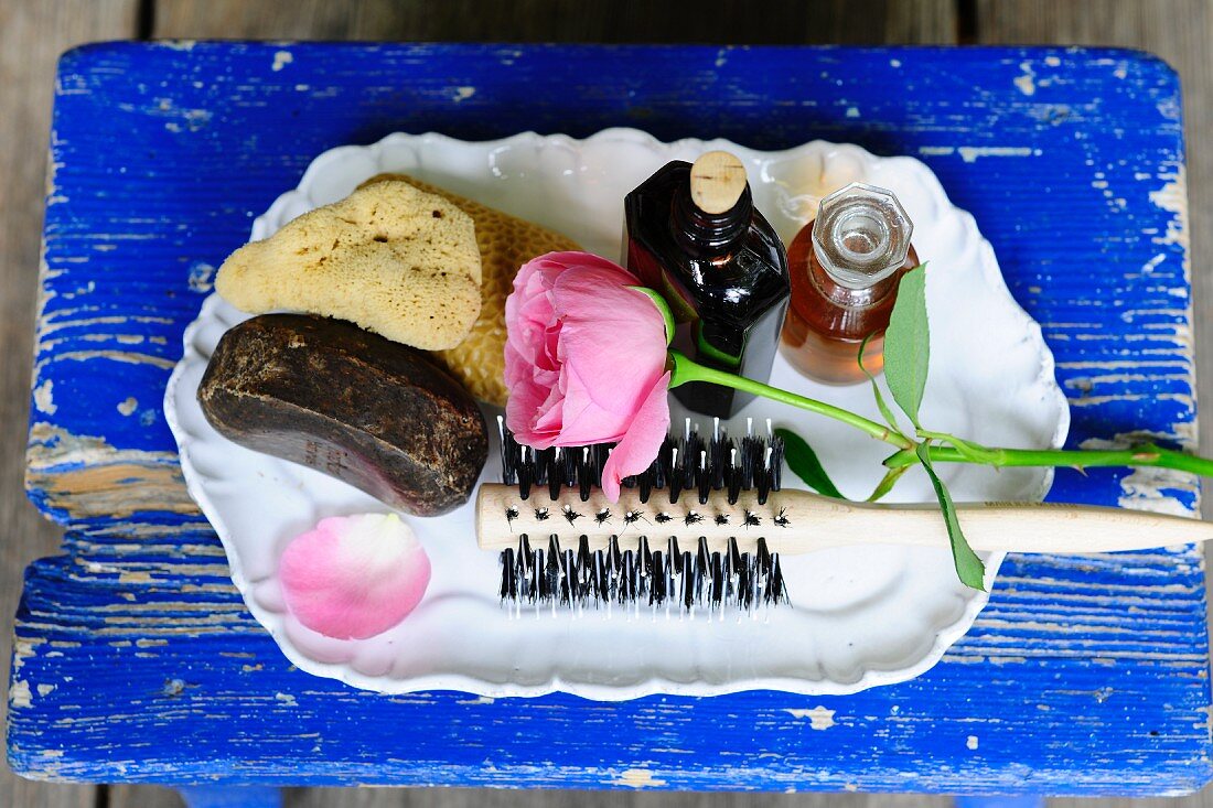 Sponge, toiletries, hair brushed and rose on white tray on blue wooden board