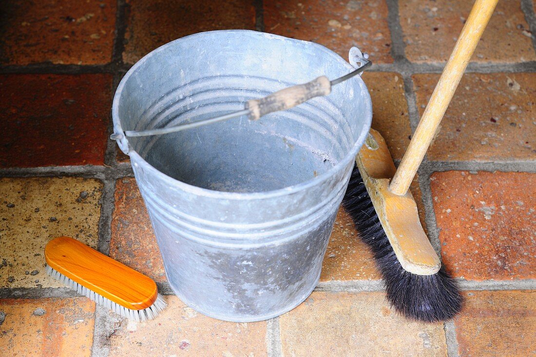 Metal bucket, broom and scrubbing brush on terracotta floor