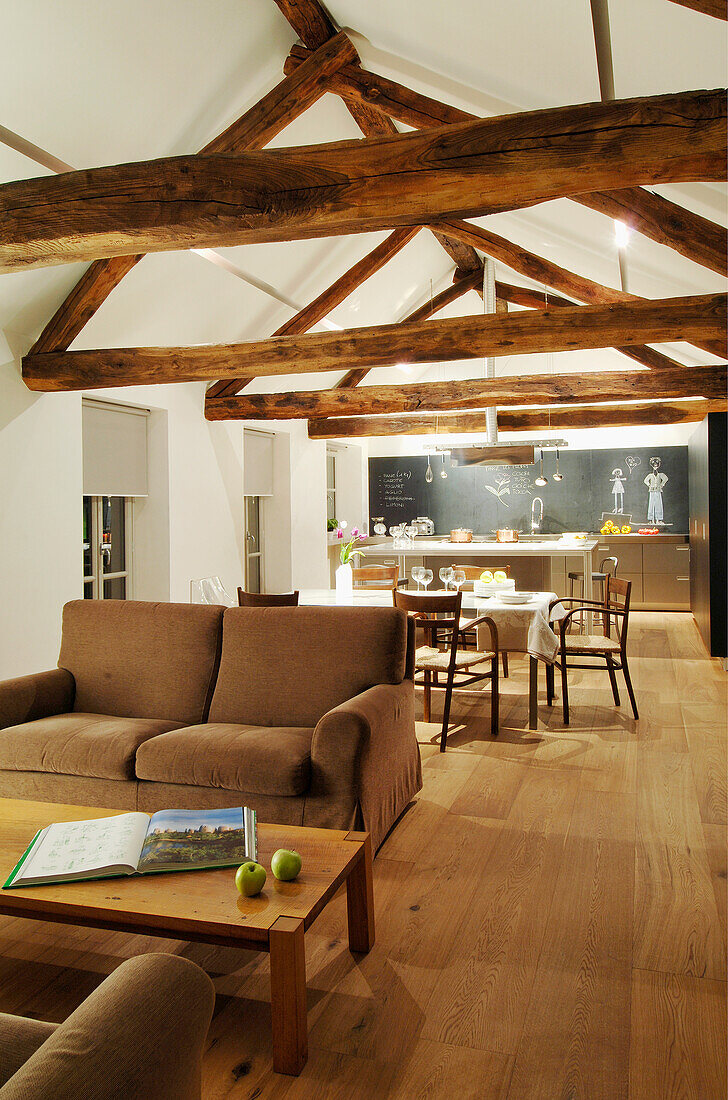 Braune Couch und Couchtisch in offenem Wohnraum mit Holzbalken