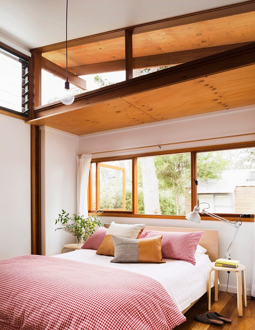 Bright bedroom with Asian and European flair; Double bed with red and white checked bed linen and pillows in front of a window hinge