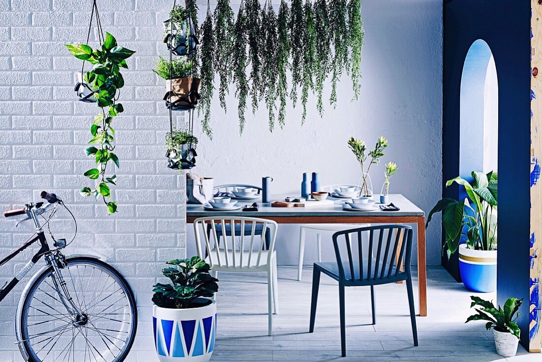 Gedeckter Tisch in kühlem, blauem Ambiente mit Grünpflanzen und Rundbogendurchgang